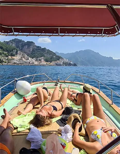 A happy family relaxing and sunbathing on a private Gozzo boat during a customized tour in the crystal clear waters of Amalfi, enjoying an exclusive tailored excursion along the Amalfi Coast with Frasil Charter.